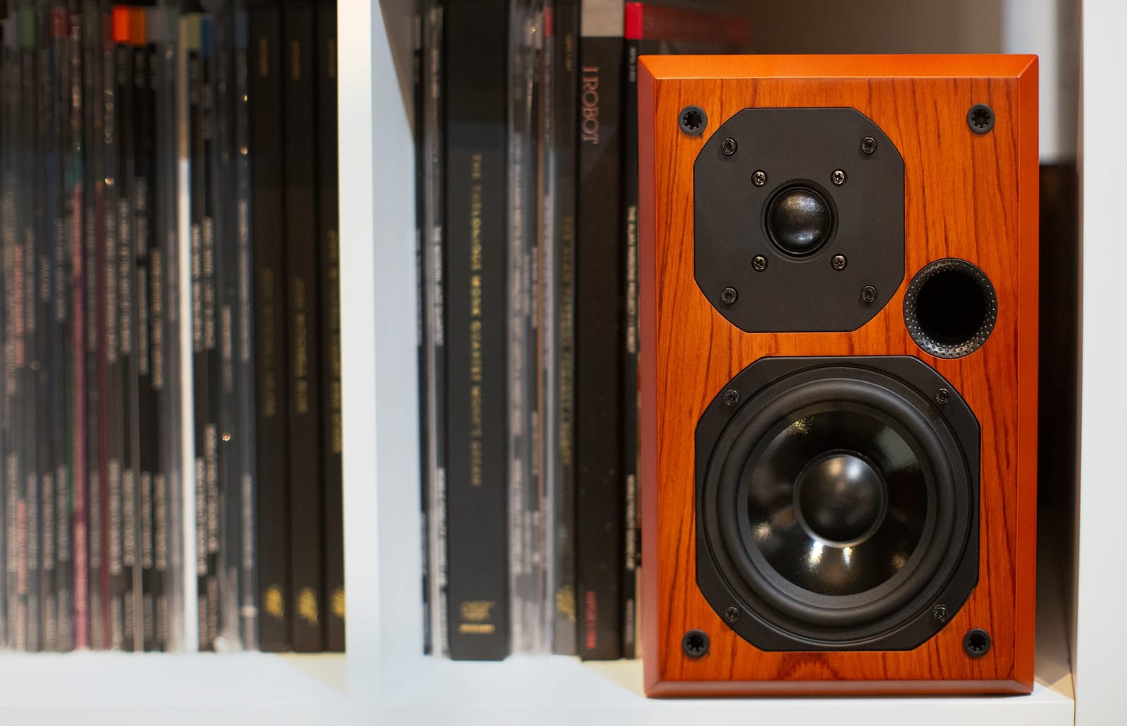 Wooden speaker with black components on a white surface with books in the background